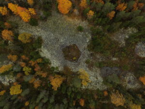 Drone-kuva Rakanmäen röykkiöiden yläpuolelta syksyllä. Osa puist kellertää ja keskellä kuvaa näkyy Rakanmäen viisikulmainen röykkiörakennelma