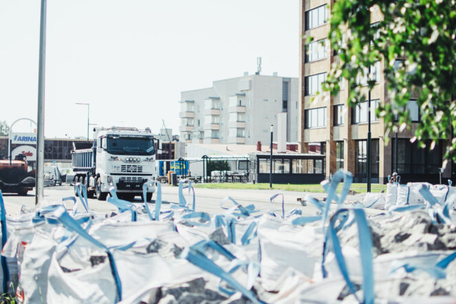 tietyömaa-alue etualalla katukiviä säkeissä ja kuorma-auto taustalla kerrostaloja