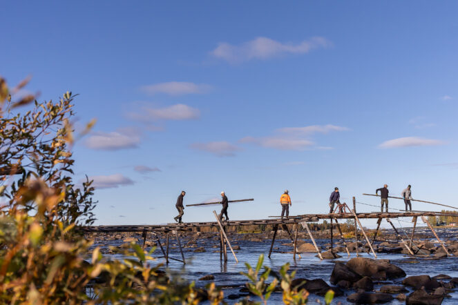 Ihmiset kantavat krenkun eli kalastuslaiturin puita syksyisessä maisemassa Tornionjoella