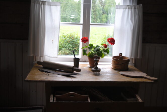 Sisäkuva Kolarin kotiseutumuseon näyttelystä. Ikkunanvieruspöydällä punainen pelargoni ja leivontavälineitä.